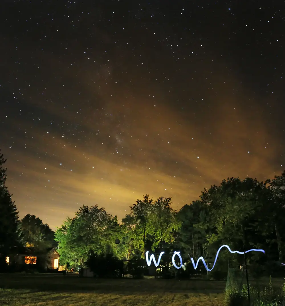 A slow exposure of a starry landscape with the word 'WOW' light painting.